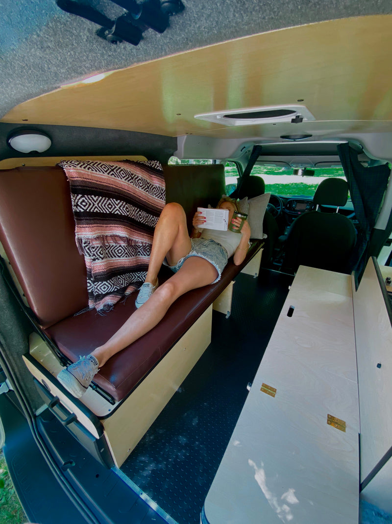 Relaxing in an RV rental: a woman reads on a cozy bench in her custom camper van, embracing van life travel. — photo 10