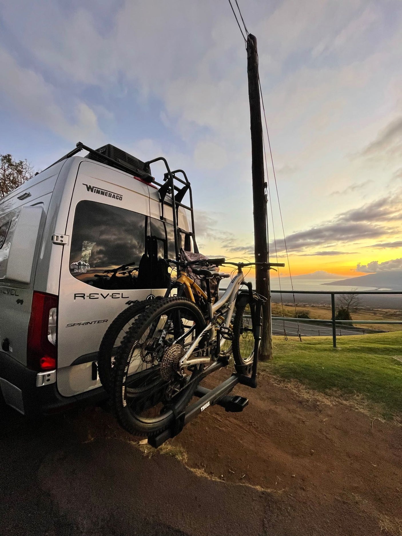 RV rental adventure: Winnebago van with mountain bikes overlooking a vivid sunset and scenic ocean view.