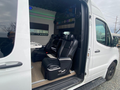 Experience luxury RV rental: custom van interior featuring executive seats, ambient lighting, and entertainment screen.