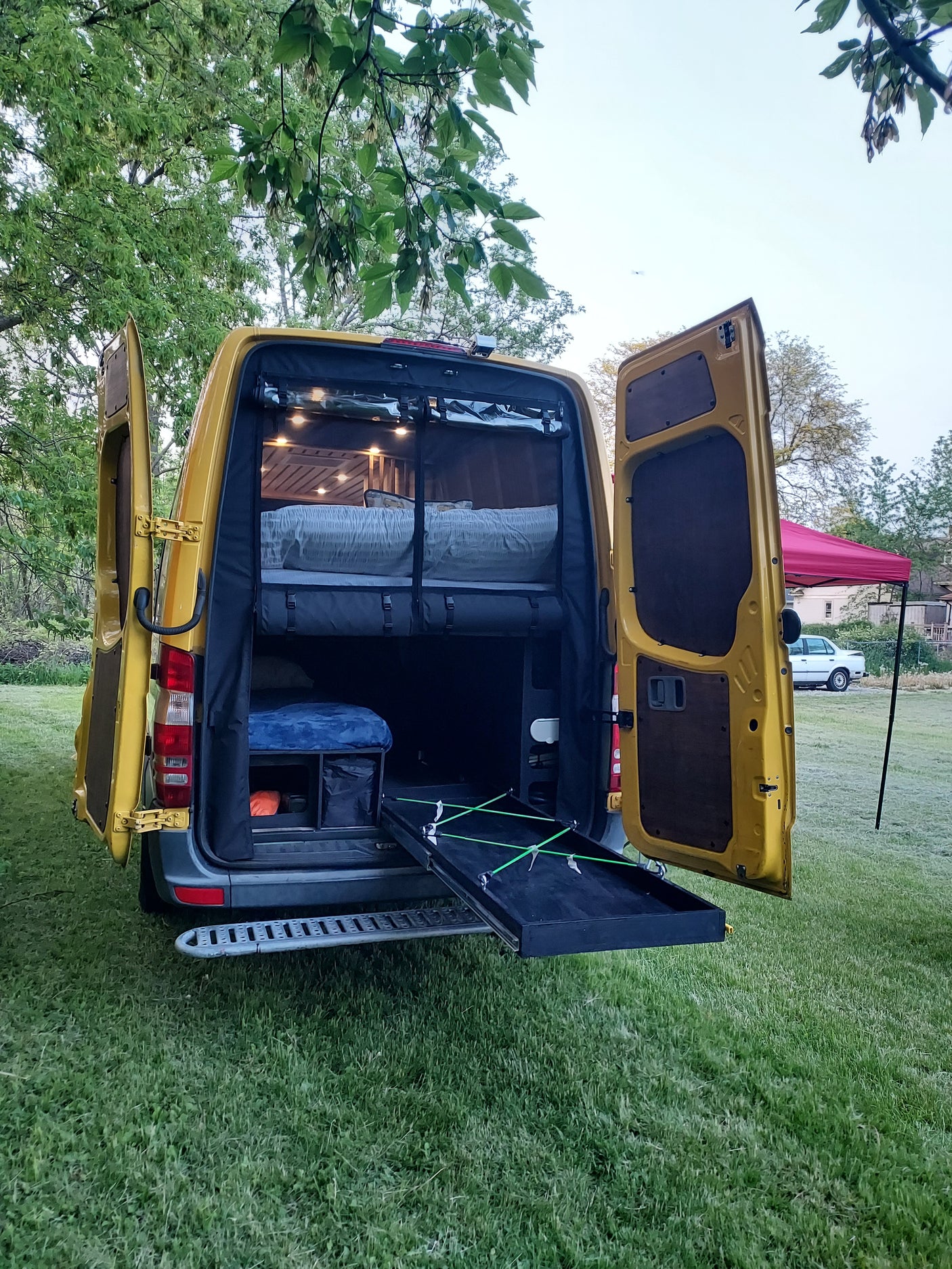 Open rear of a yellow camper van, revealing its interior setup with a bed, storage, and ambient lights. Great for an RV rental adventure.