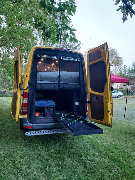 Open rear of a yellow camper van, revealing its interior setup with a bed, storage, and ambient lights. Great for an RV rental adventure.