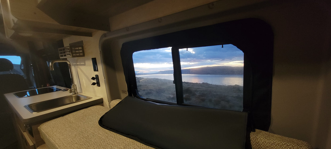 Enjoy tranquil lake views from this cozy RV rental's bed and kitchenette, offering a perfect setting for scenic road trips.