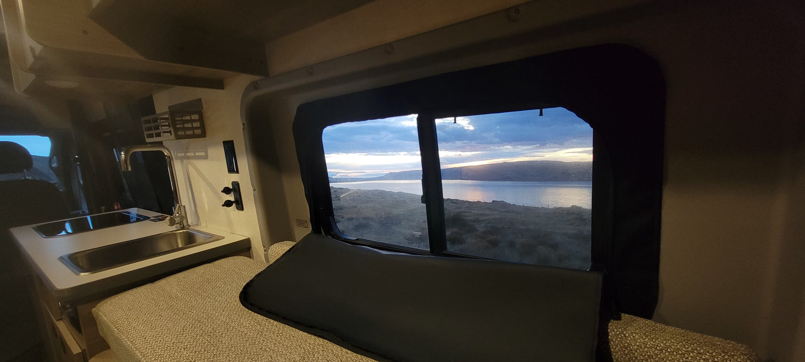 Enjoy tranquil lake views from this cozy RV rental's bed and kitchenette, offering a perfect setting for scenic road trips.