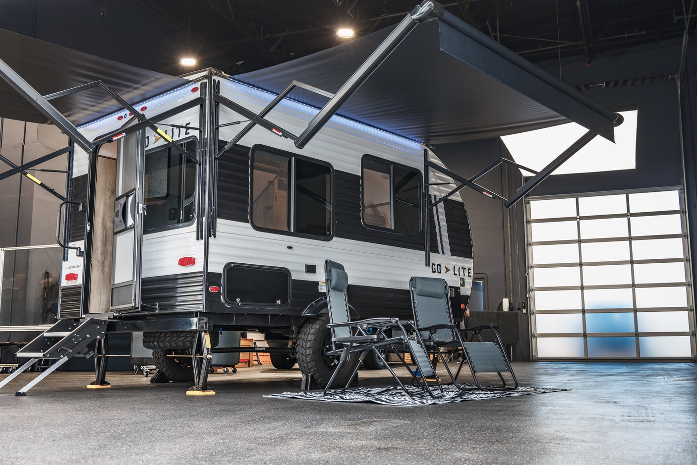 Modern Go Lite travel trailer RV rental parked indoors, with dual awnings, steps, and outdoor chairs.