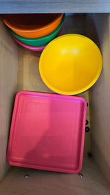 Bright plastic bowls & a pink tray in an RV rental drawer, perfect for compact kitchen storage.