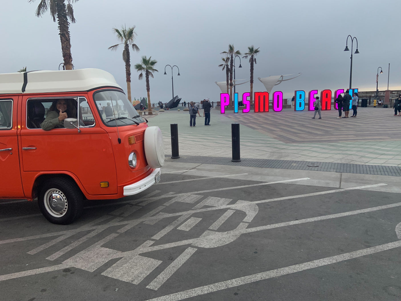 Enjoying Pismo Beach in a classic orange RV rental, with a thumbs-up from the driver and the colorful "PISMO BEACH" sign.