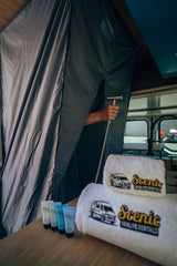 Your RV rental offers convenience: a person with a showerhead, toiletries, and Scenic Vanlife Rentals towels on the counter.