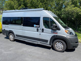 A modern light grey Ram ProMaster camper van, perfect for an rv rental, parked on a driveway with trees.
