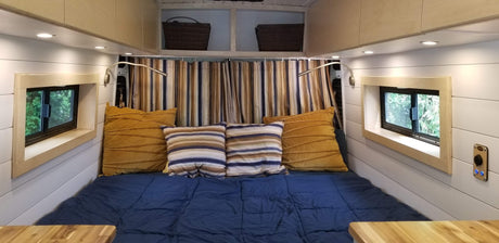 Comfortable RV rental interior with a bed, warm lighting, framed windows, and striped curtains.