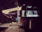 Cozy Airstream rv rental at night, with an illuminated awning and patterned outdoor mats, perfect for camping under the stars.
