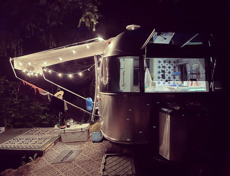 Cozy Airstream rv rental at night, with an illuminated awning and patterned outdoor mats, perfect for camping under the stars.