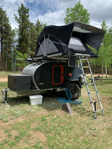An Escapod topo teardrop trailer with a rooftop tent set up for an rv rental camping adventure in a forest.