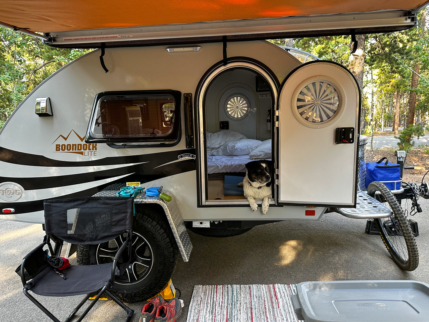 Dog relaxes in a "Boondock Lite" teardrop travel trailer, a compact RV rental, set up at a peaceful campsite.