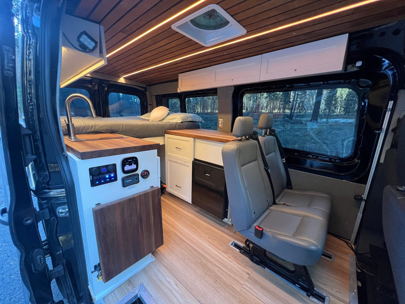 Cozy rv rental van conversion featuring a bed, kitchenette with controls, passenger seating, and a warm wood-slat ceiling. — photo 18