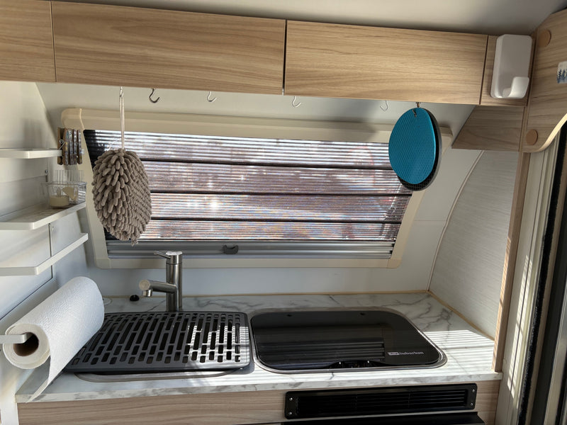 RV rental kitchen: functional space with sink, covered stove, window blinds, and overhead storage with hanging hooks. — photo 3