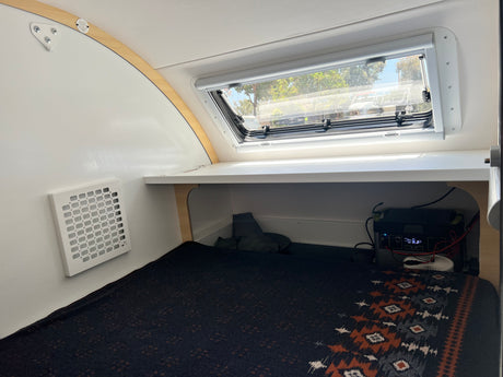 Small RV rental interior: cozy bed with patterned blanket, large window, and portable power station.