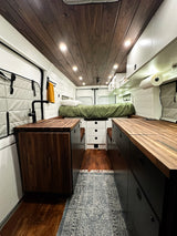 Explore this modern RV rental interior featuring a wooden ceiling, cozy bed, and functional kitchen setup.