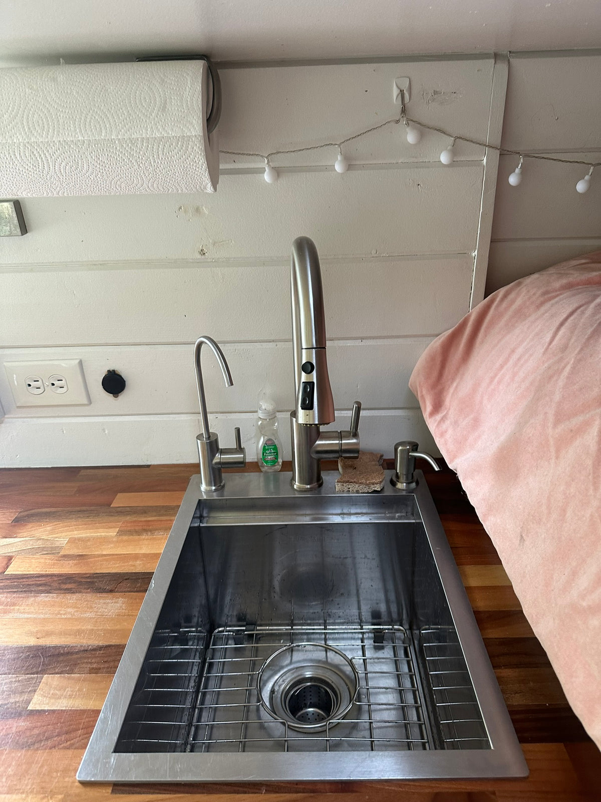 This compact kitchen in an RV rental features a stainless steel sink, wood counter, overhead paper towels, and cozy lighting. — photo 11