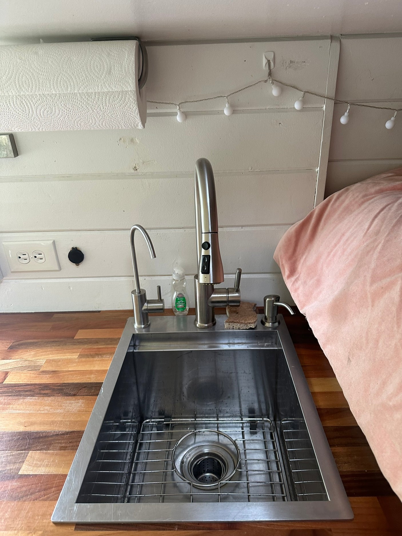 This compact kitchen in an RV rental features a stainless steel sink, wood counter, overhead paper towels, and cozy lighting.