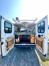 Open rear doors of this custom rv rental van show a wood interior, bed, storage, and a Road Shower 4 on the roof.