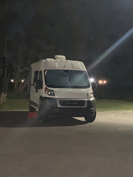 White camper van, resembling an RV rental, parked on asphalt at night.