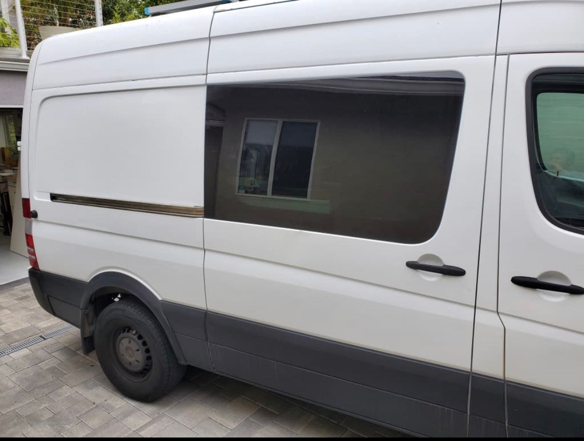 White van, ideal for RV rental, featuring a large sliding door and dark tinted side window. Parked on outdoor pavers.