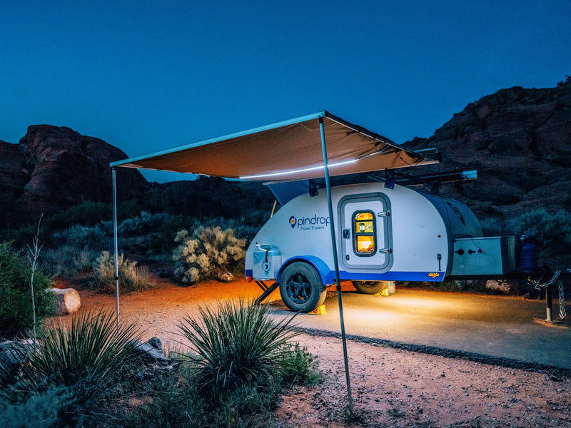 Illuminated teardrop RV rental with awning at a tranquil desert campsite under a deep blue night sky. — photo 7