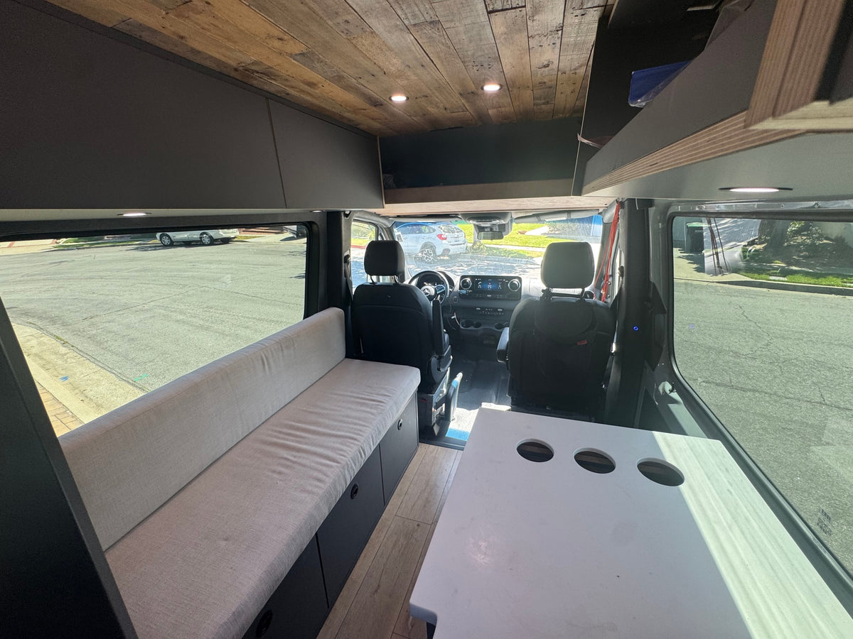 Step into this cozy RV rental camper van, featuring a long bench seat with storage, a plank wood ceiling, and a versatile table. — photo 7