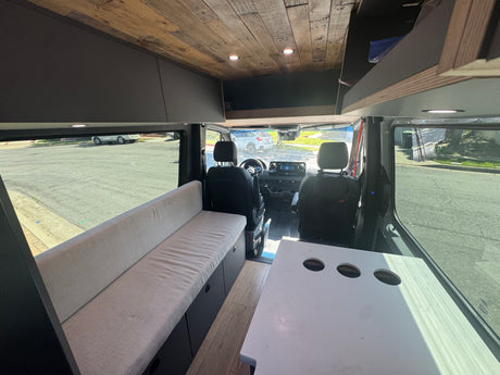 Step into this cozy RV rental camper van, featuring a long bench seat with storage, a plank wood ceiling, and a versatile table.