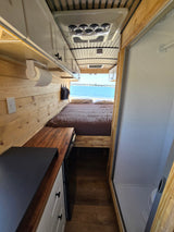 Cozy rv rental interior showcasing a full bed, compact kitchen, and separate shower. Stunning ocean view!