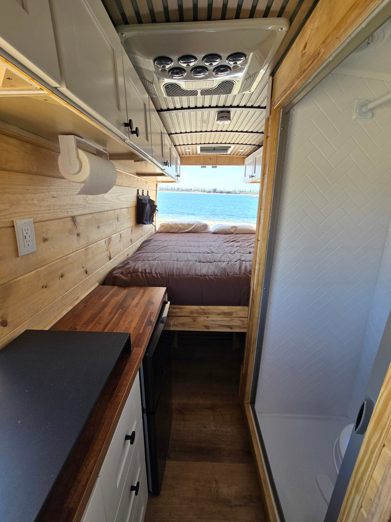  & power outlets.|Cozy RV rental camper van interior: a bed with wood walls opens to a beautiful beach and ocean view.|RV rental solar power system: Victron charge controllers — photo 6
