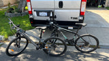 An RV rental van with a bike rack holds two bicycles, a gray COSTIC and a black SYBIC, ready for travel.