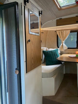 Experience a cozy **RV rental**: compact interior with bench seating, a small table, and a screen door for ventilation.