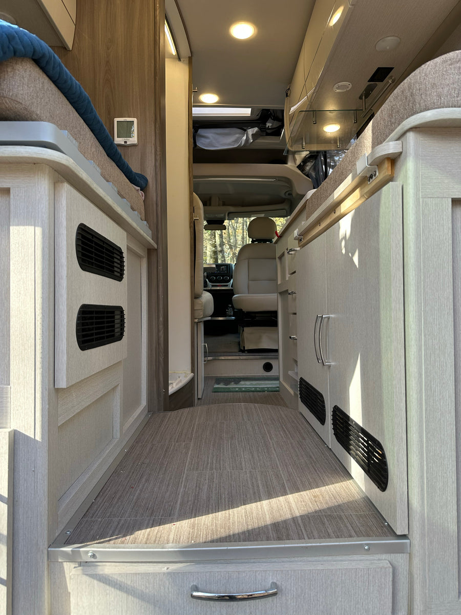 Spacious RV rental interior featuring light wood cabinetry, a sleeping area, and a clear view to the driver's cabin and outdoors.