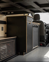 Compact rv rental van interior with modern black textured modular cabinets, integrated fridge, and light wood trim details.