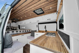 Cozy rv rental van interior featuring a warm wooden ceiling, compact kitchen with wood counters, bed, and white built-in storage.