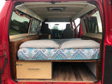 Red van interior converted to a cozy camper, featuring a full bed, storage, and front cabin access – ideal for rv rental.