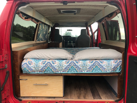 Red van interior converted to a cozy camper, featuring a full bed, storage, and front cabin access – ideal for rv rental.