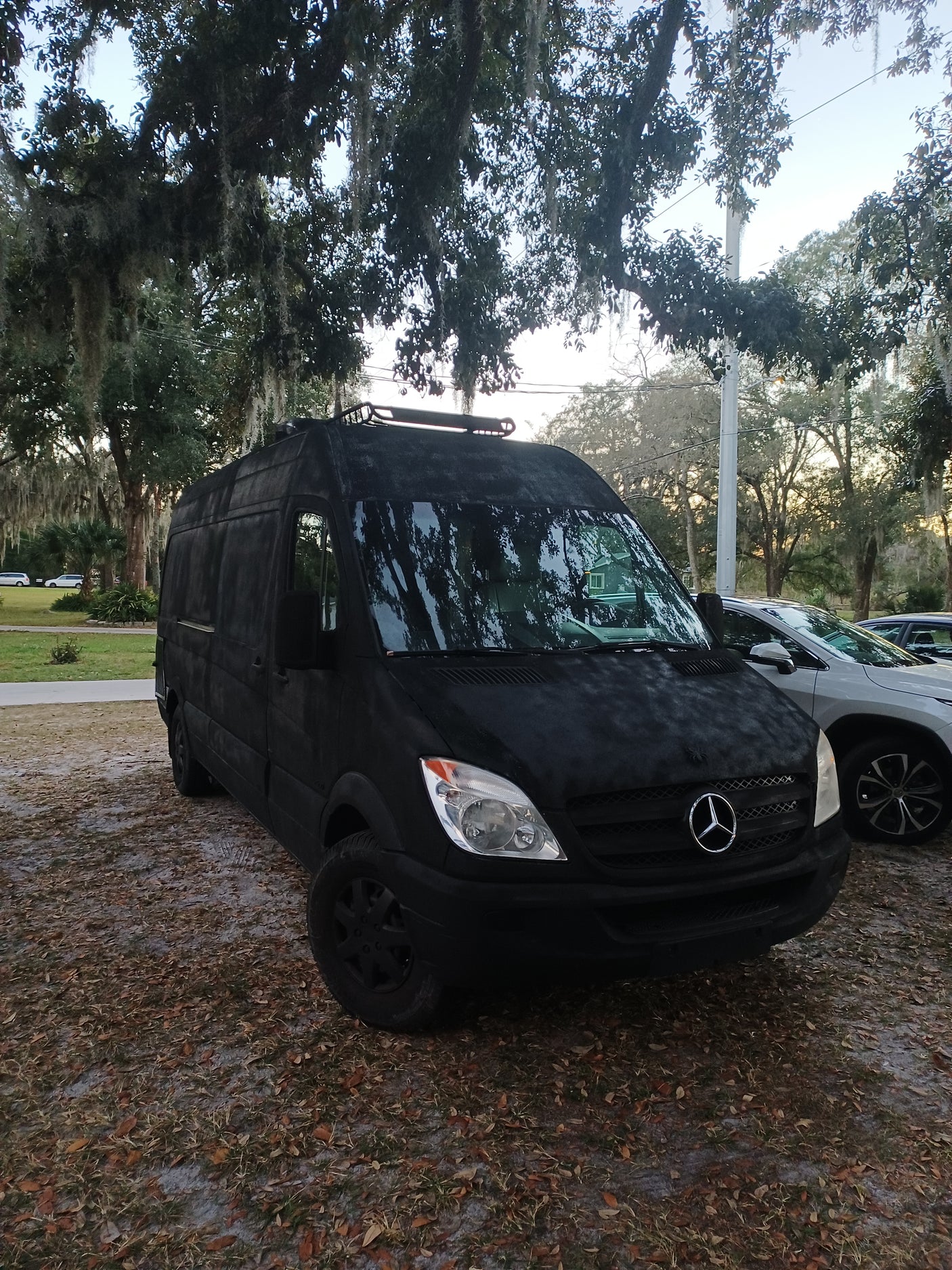 Black Mercedes Sprinter van, ideal for rv rental & van life adventures, parked by mossy trees.
