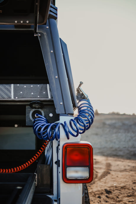 Close-up of an RV rental's rear utility area: blue coiled air/water hose, port, orange wire, and red taillight. Ideal for adventure.