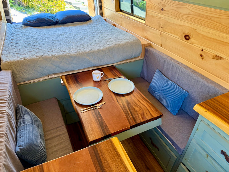 Cozy RV rental interior featuring a raised bed, dining table set for two, and comfortable bench seating. — photo 6