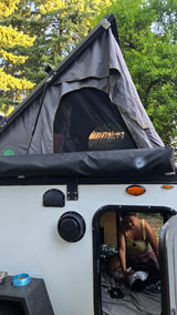 This RV rental is pet-friendly! A cat watches from the rooftop tent, as a person organizes inside the camper.