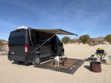 RV rental van with awning, two dogs on a rug, picnic table, and fire pit at a desert campsite. Ideal for outdoor adventures!