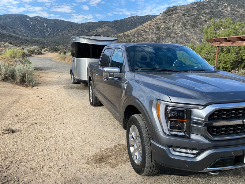 A gray Ford F-150 truck tows a silver Airstream Basecamp RV on a dirt road in the mountains. Explore with an rv rental! — photo 16