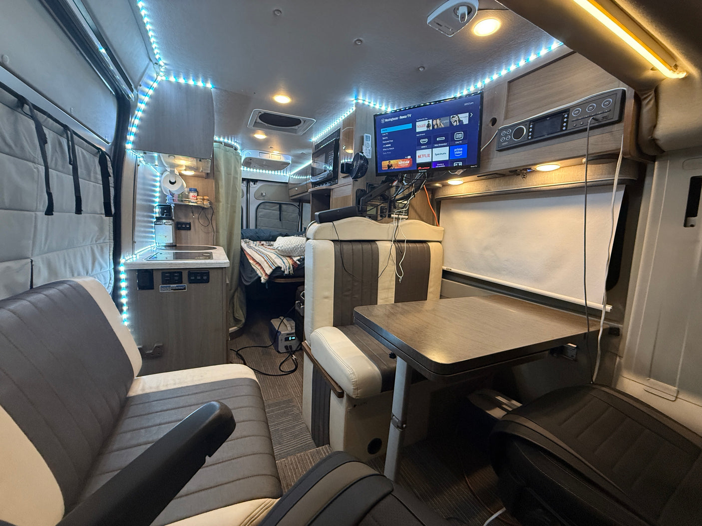 Explore this RV rental's well-equipped interior: cozy seating, table, TV, kitchen, and sleeping area, ready for travel.