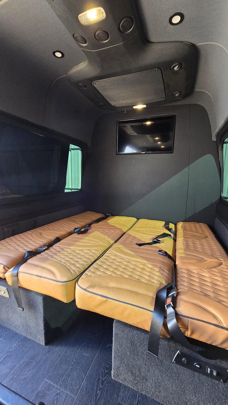 Custom tan quilted seats in this RV rental's interior. Seats convert to beds, with safety belts, a TV, and dark wood floor.