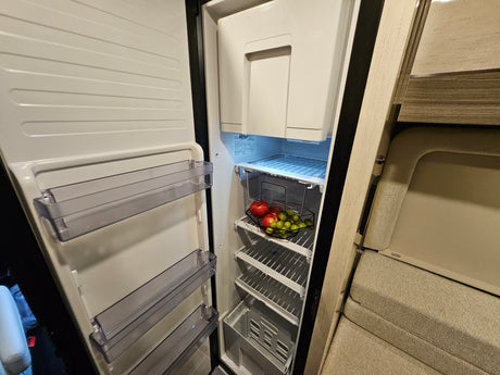 Open RV rental refrigerator with fresh fruit, showing organized interior shelves and door bins.