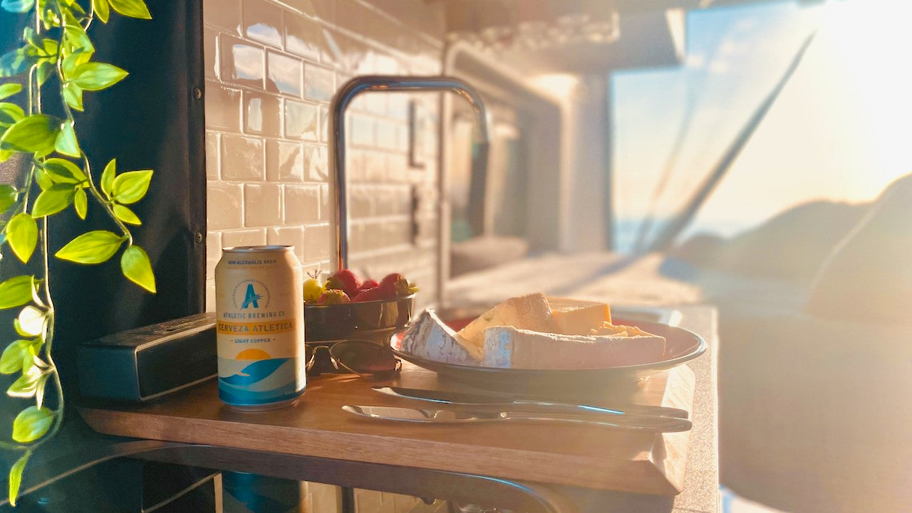 Cozy RV rental interior with a non-alcoholic beer, cheese, and fruit, bathed in golden hour light. Travel bliss!