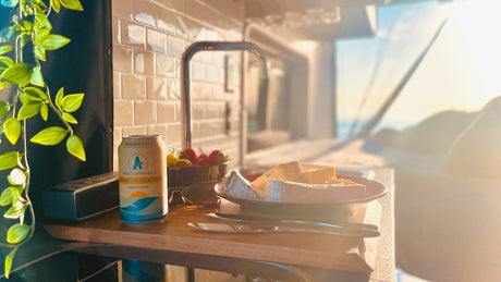 Cozy RV rental interior with a non-alcoholic beer, cheese, and fruit, bathed in golden hour light. Travel bliss!