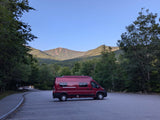 A red camper van, ideal for an rv rental adventure, parked in a scenic mountain lot surrounded by lush trees.